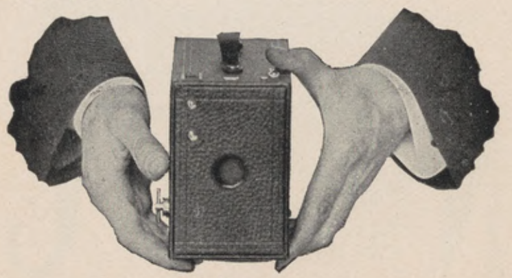 Hands holding the Brownie camera upright for a vertical exposure.