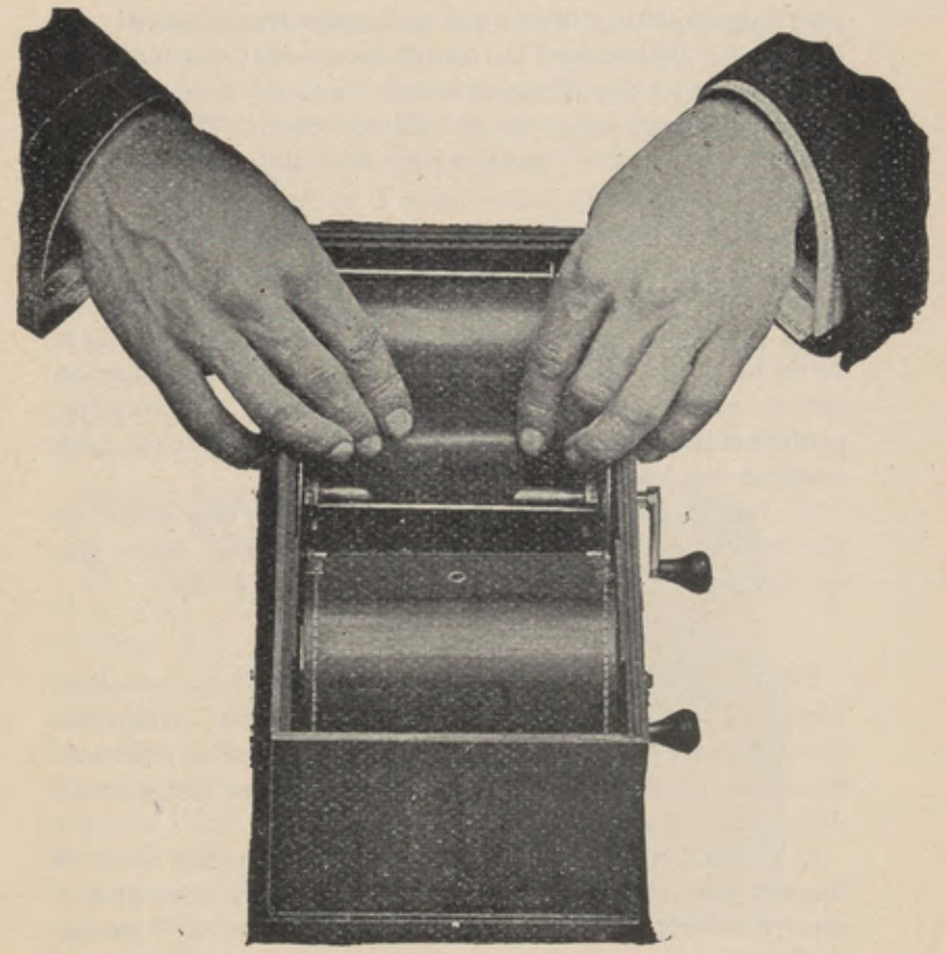 Hands winding the light-proof apron on the spindle of the loading box.